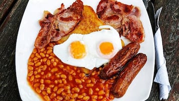A plate of beans, sausages, bacon, and eggs on a wooden table.