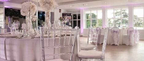 A banquet hall with round tables, clear chairs, and white floral centerpieces.