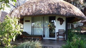 A thatched-roof hut with a sliding glass door, a wooden bench, and a chair outside. - Caprivi River Lodge (Katima Mulilo)