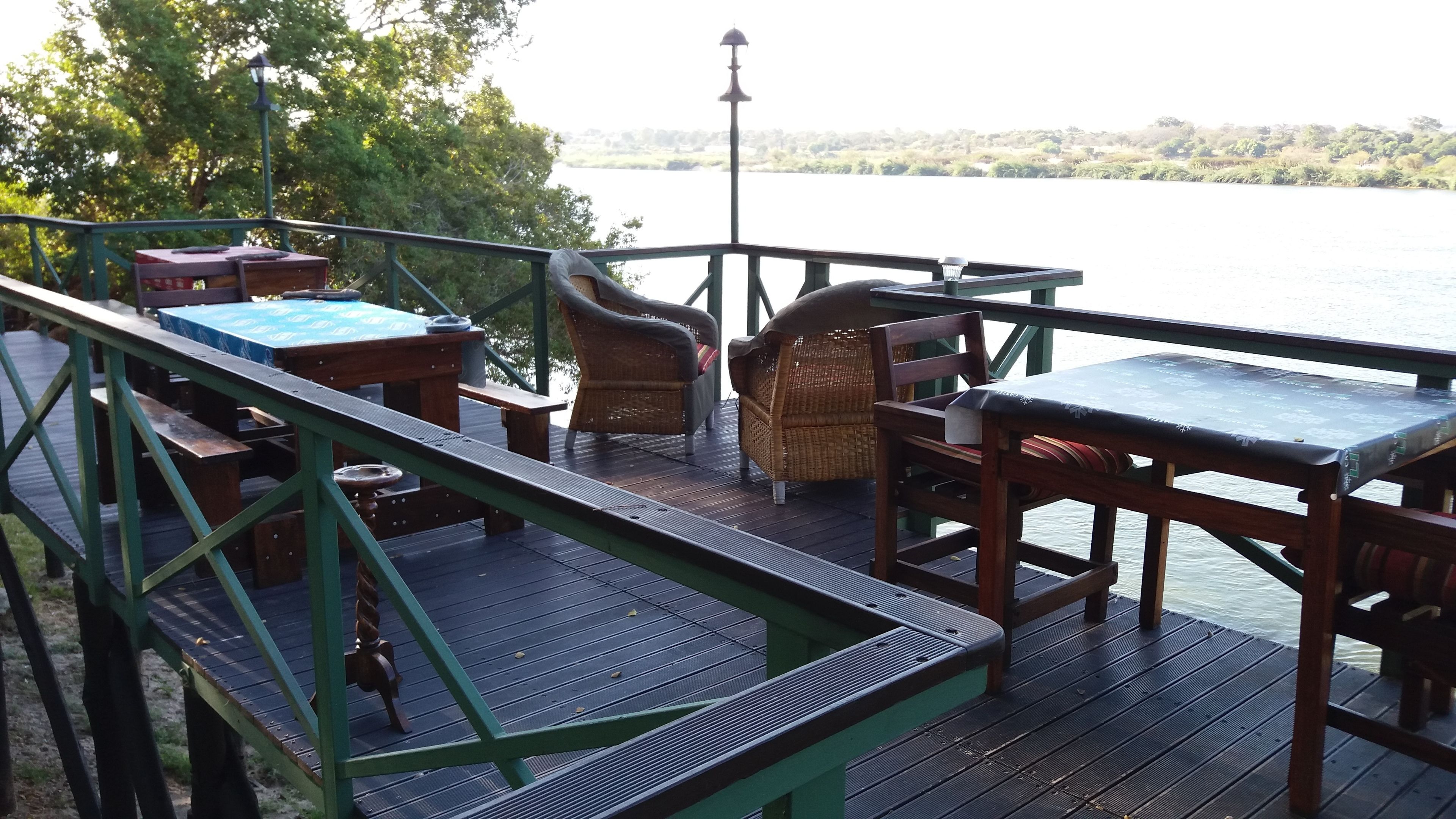 A wooden deck with outdoor furniture, including a table and chairs, overlooking a body of water.