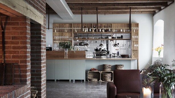 A modern kitchen with exposed brick, wooden shelves, and a central island. - Wanås Restaurant Hotel (Knislinge)