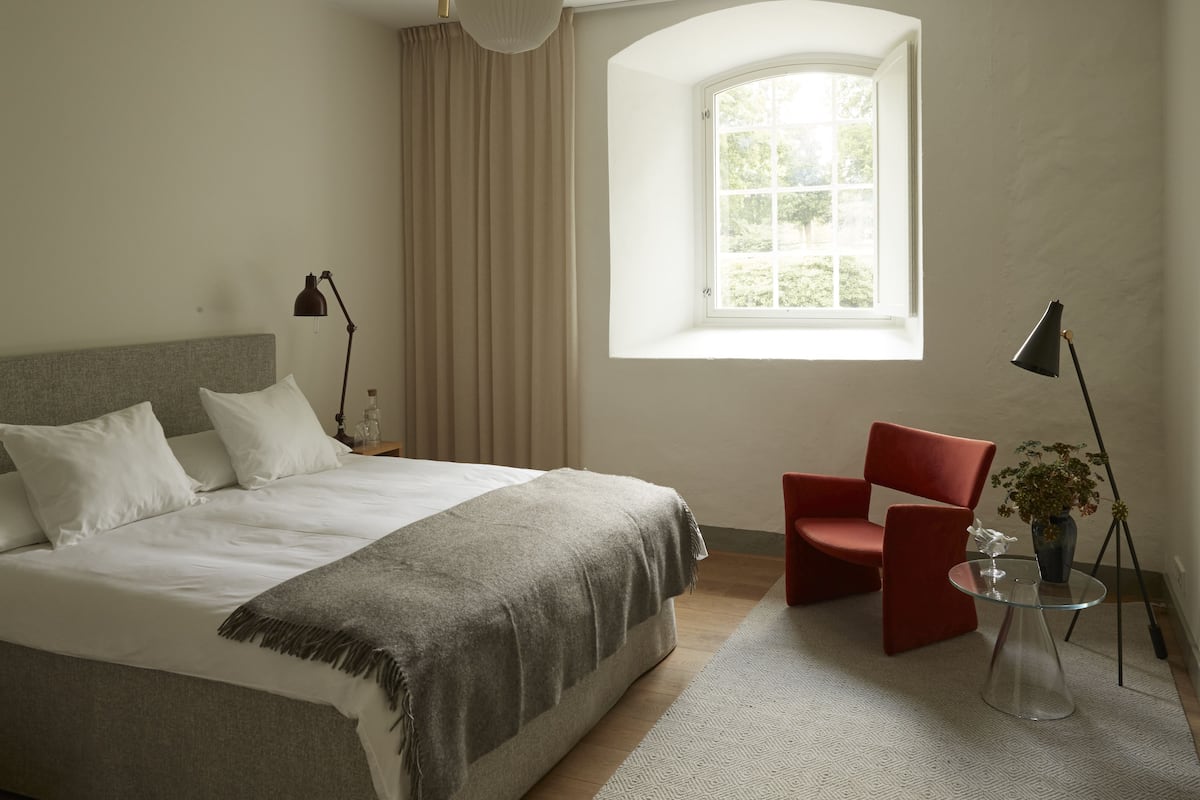 A bedroom with a bed, a window, a chair, and a lamp.
