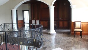 A grand hall with a marble floor, white columns, and a black wrought iron railing.