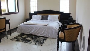 A bedroom with a bed, a chair, a nightstand, a bedside table, and a window.