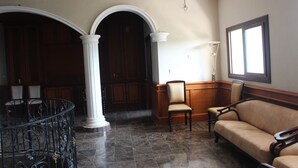 A spacious lobby with a marble floor, a wooden reception desk, a sofa, and a large window providing natural light.