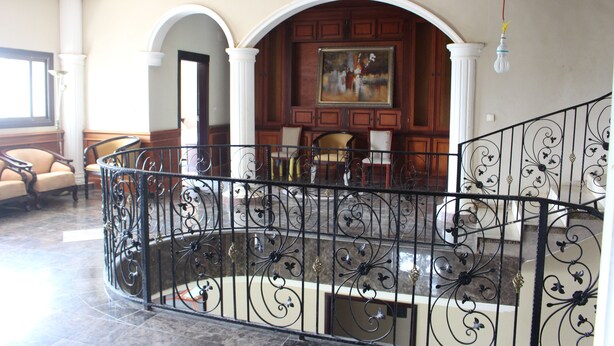 A spacious lobby with a curved black metal railing, a wooden reception desk, and a painting on the wall.