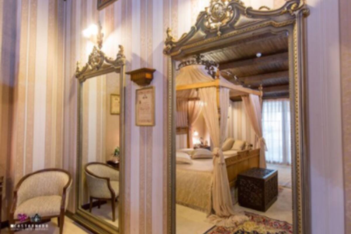 Un dormitorio con una cama con dosel, un espejo grande y ornamentado, una silla y una mesita de noche.