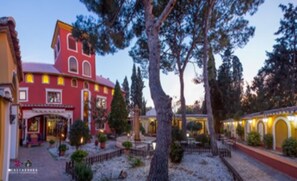 A red building with a balcony, surrounded by trees and a gravel path. - Masía de Lacy Hotel (Museros)