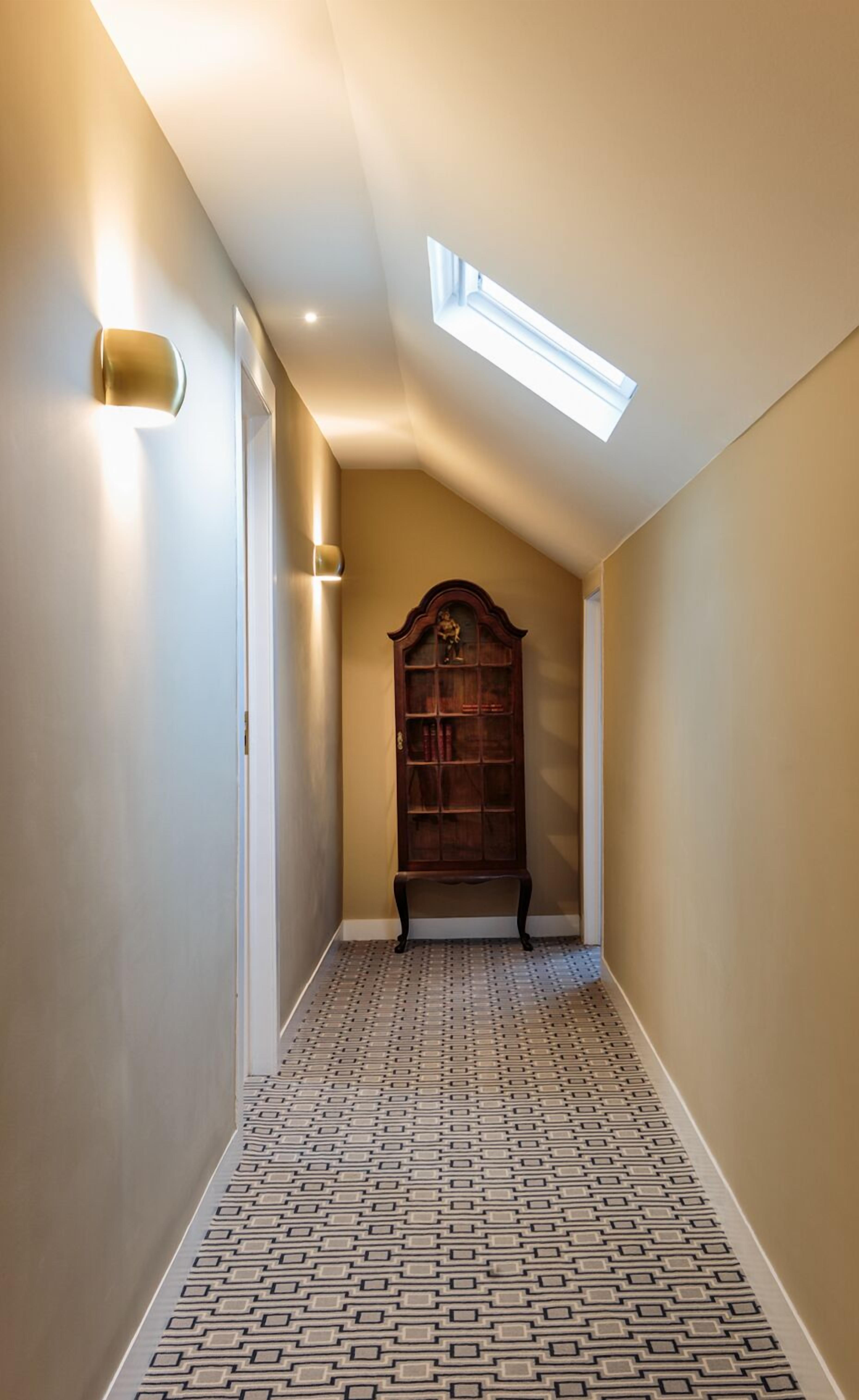 A narrow hallway with patterned flooring, a wooden bookcase, and a skylight.