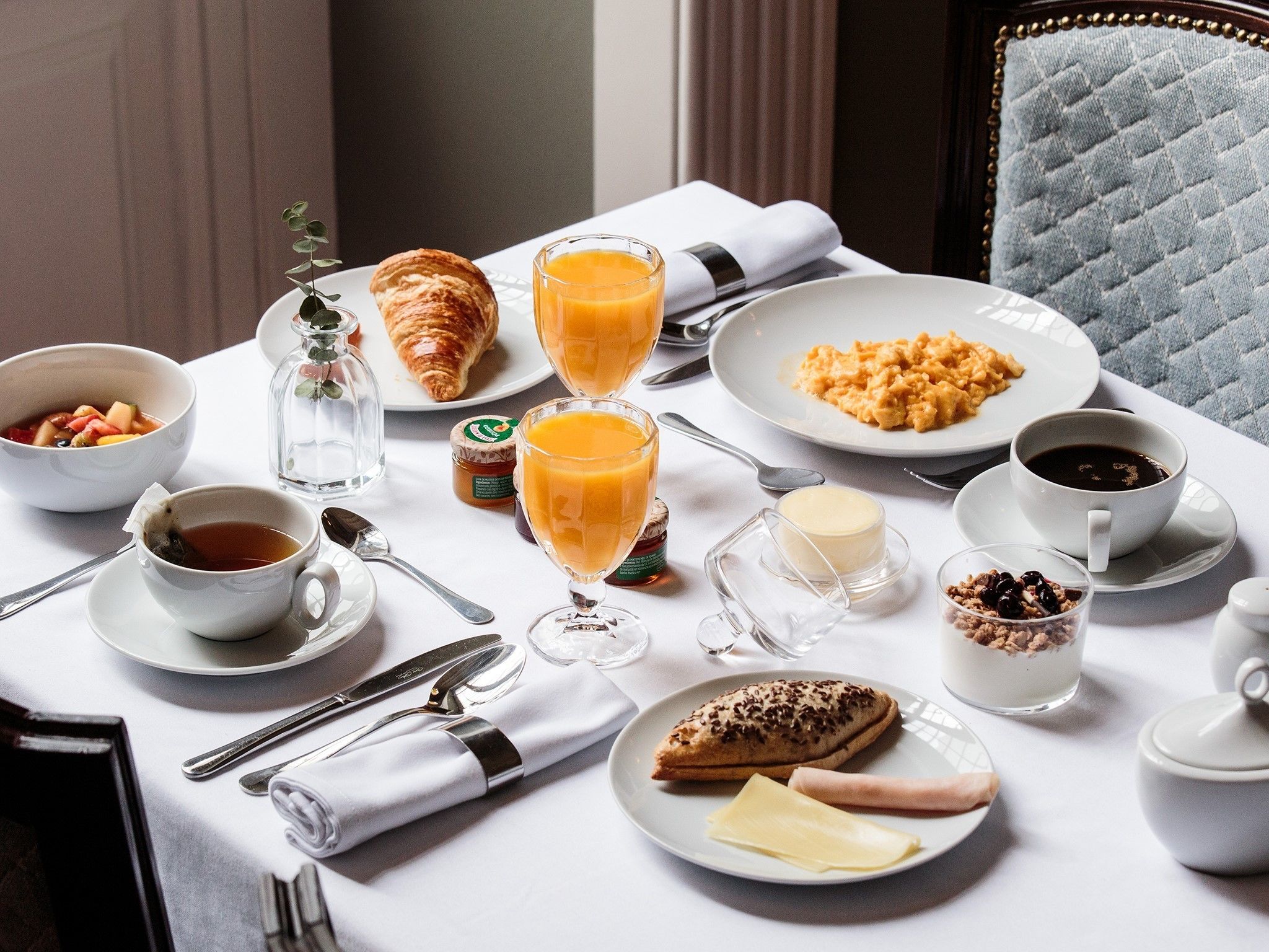 A breakfast setting with croissants, fruit, scrambled eggs, orange juice, coffee, and a variety of spreads on a table.