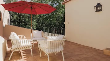 Een terras met twee witte stoelen en een rode parasol.