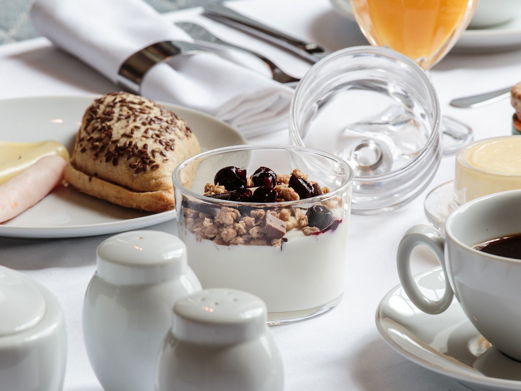 A breakfast setting with a glass dessert, a pastry, and a cup of coffee on a table.
