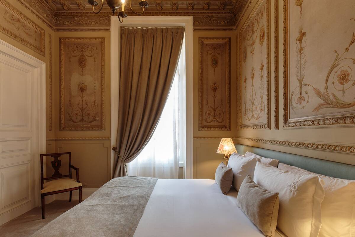 A hotel room with a large bed, a chair, a lamp, and ornate wall decorations.