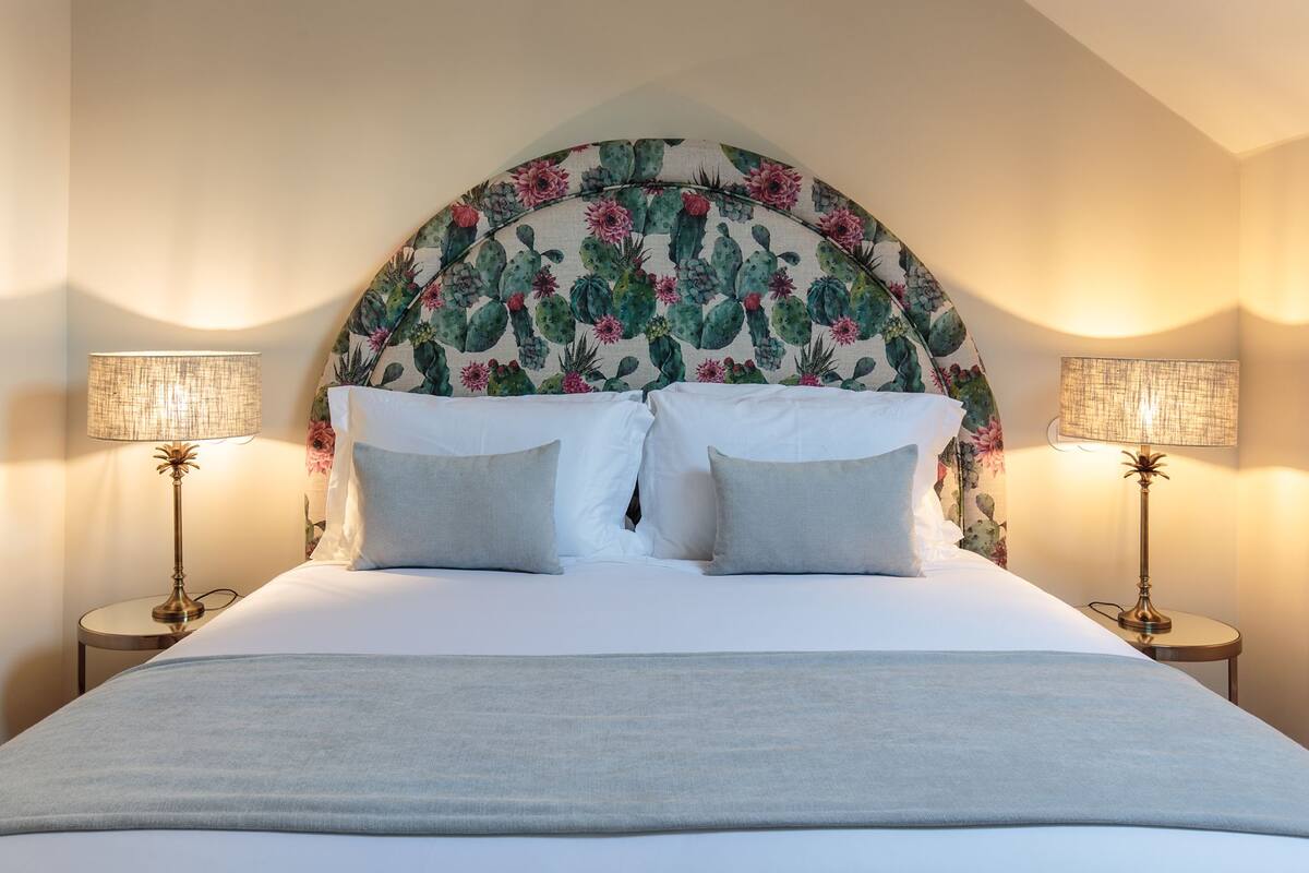 A bed with a floral headboard, two bedside lamps, and a light-colored bedspread.