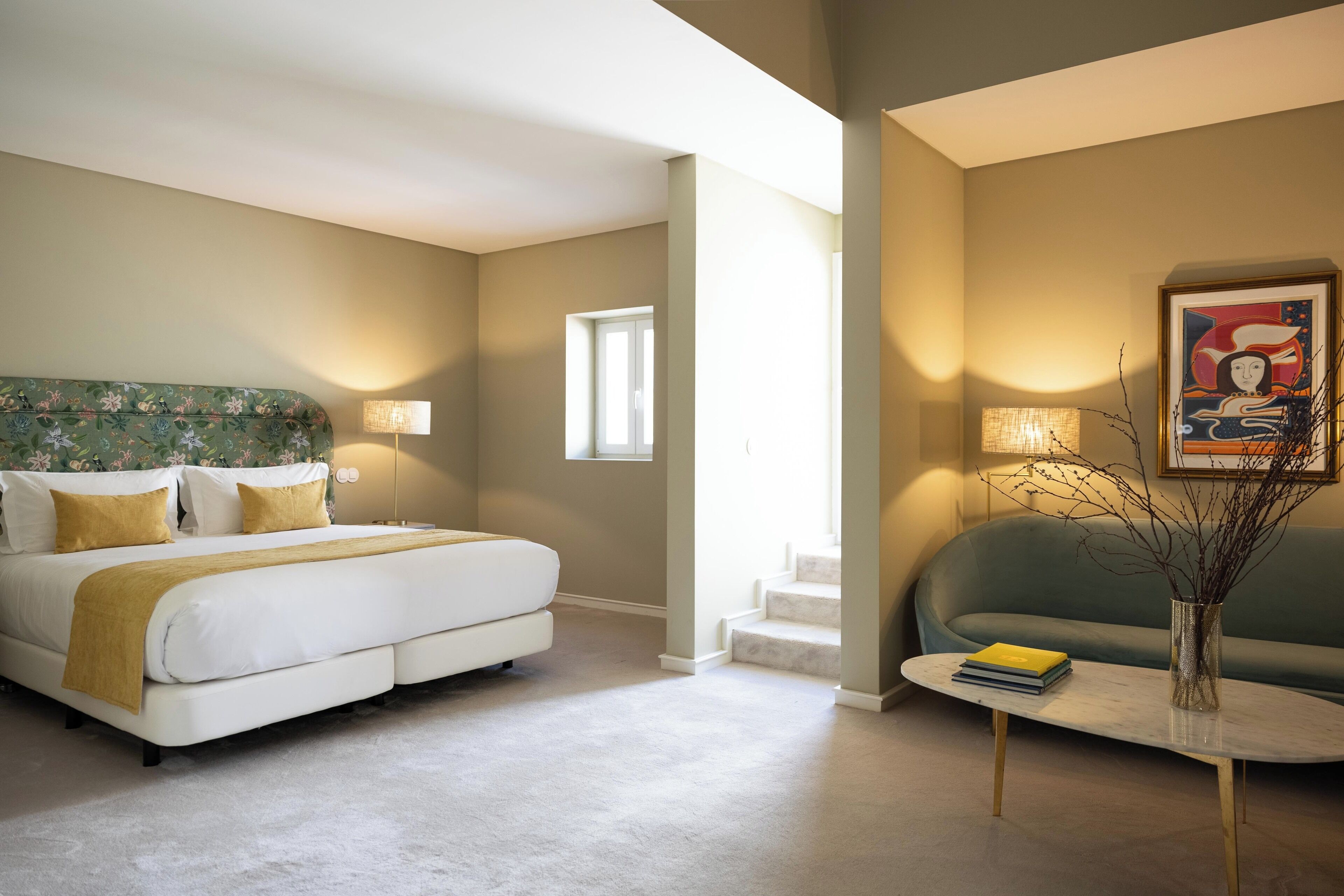 A hotel room with a bed, a sofa, a coffee table, and a painting on the wall.