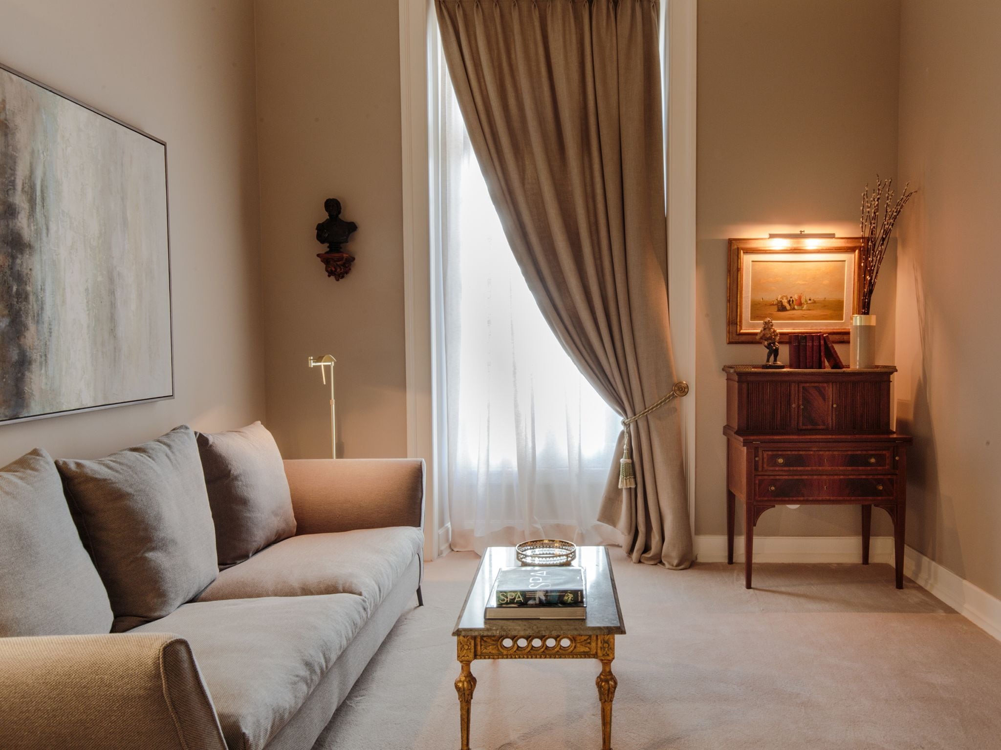 Una sala de estar acogedora con un sofá, una mesa de centro con libros, una mesita auxiliar, una lámpara y un espejo.