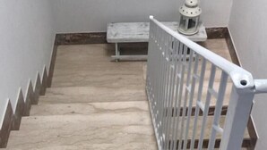 Una escalera con barandilla blanca, un reloj de pared y una mesita con lámpara.