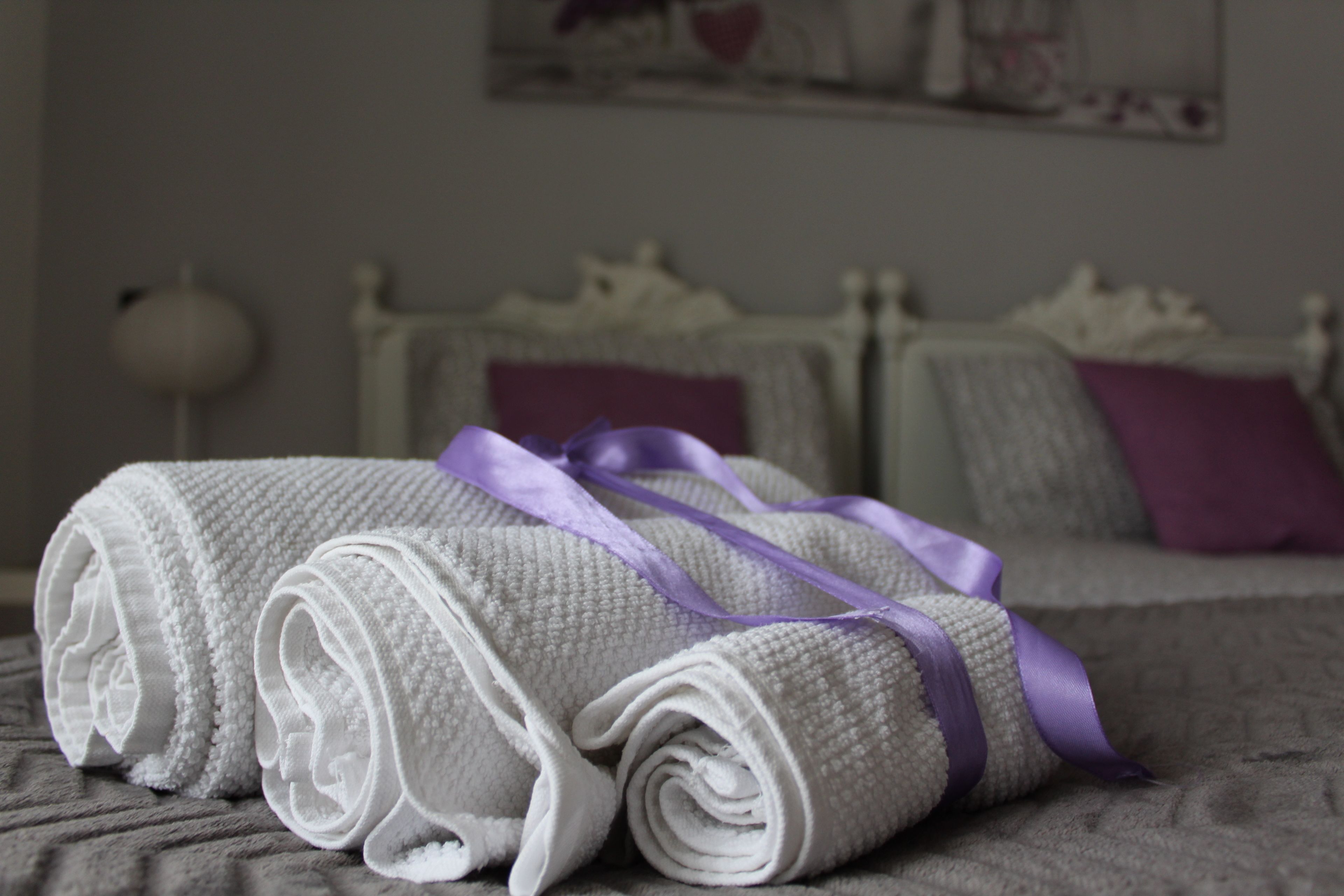 A neatly made bed with a purple ribbon, a white lamp, and a painting on the wall.