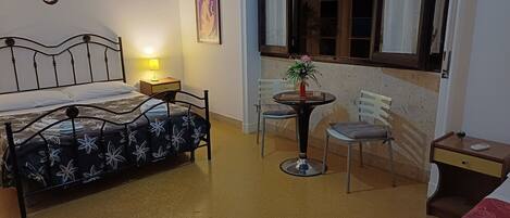 A bedroom with a bed, bedside table, lamp, chair, and a small table with a plant.