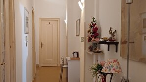 A hallway with a wooden floor, white walls, and a door at the end. There are wall-mounted lights, a small table with a lamp, and a globe on a stand. - Da Mary Guest House (Palermo)