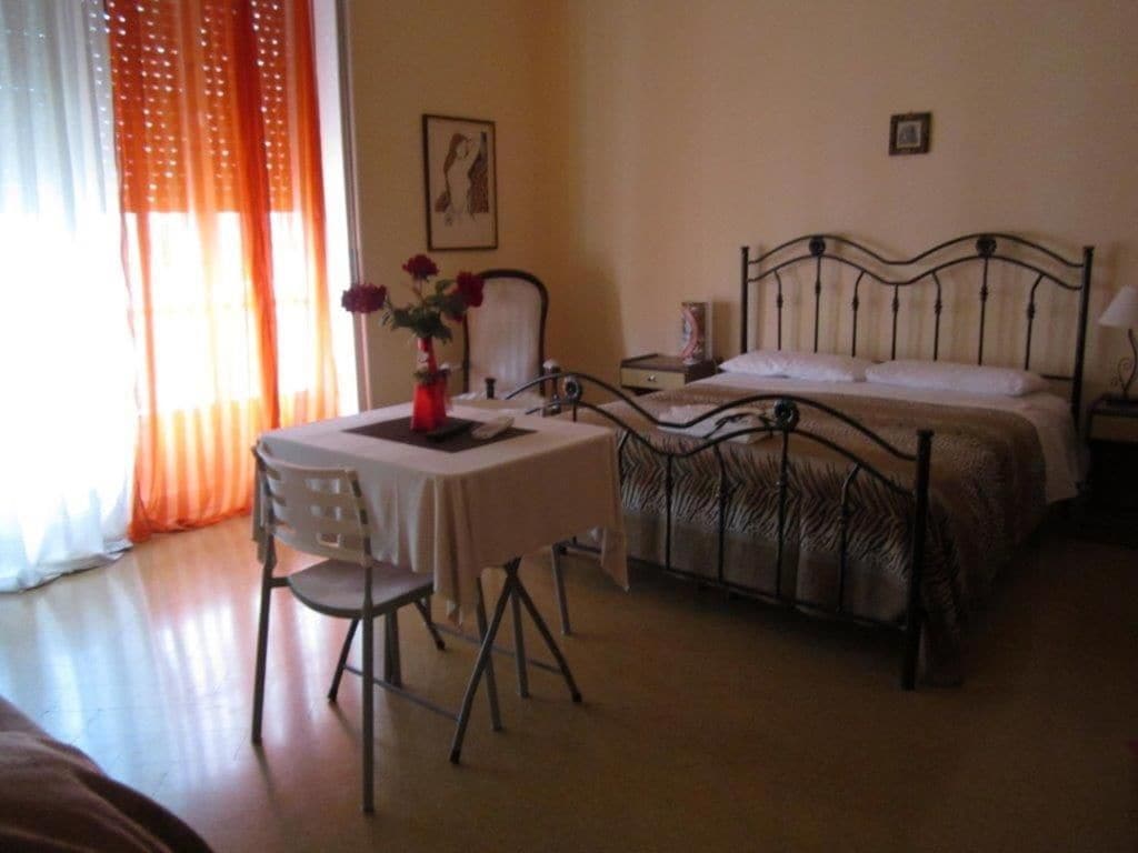 Un dormitorio con una cama, una mesita de noche, una silla y una ventana con cortinas.