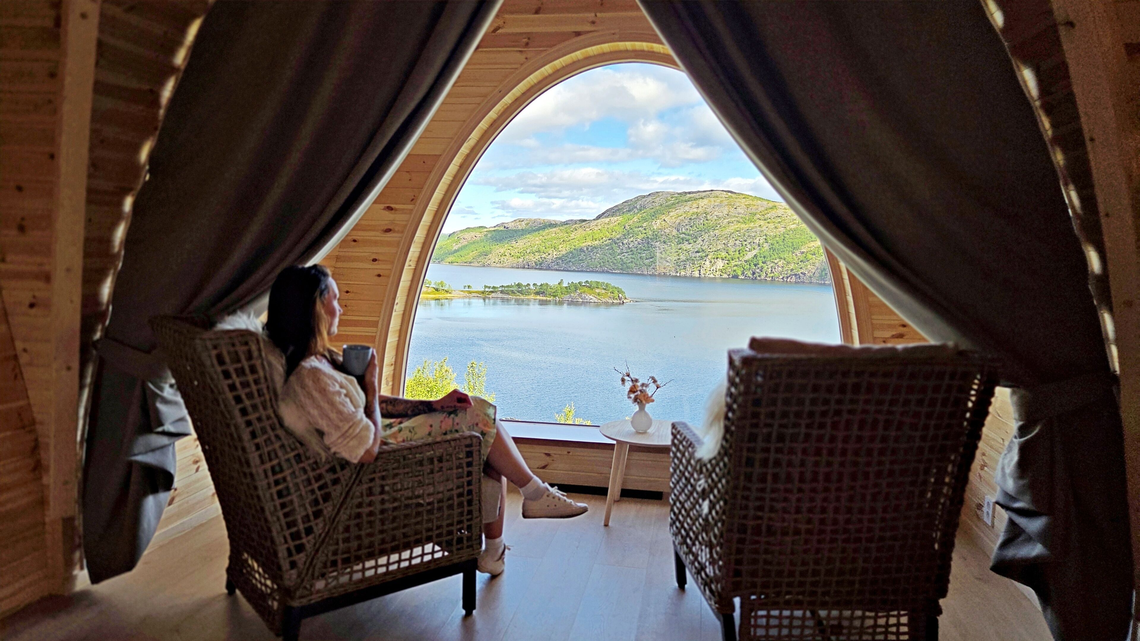 A cozy room with a large arched window overlooking a lake and hills.