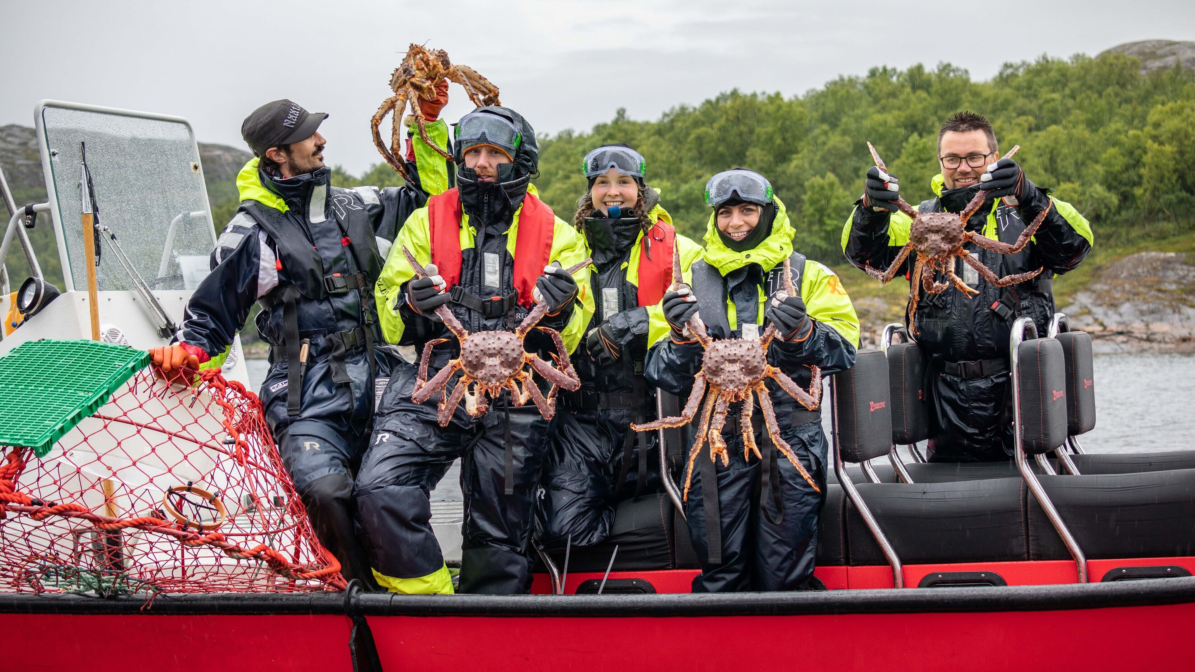 A group of people on a boat holding large crabs, wearing safety gear and life jackets.