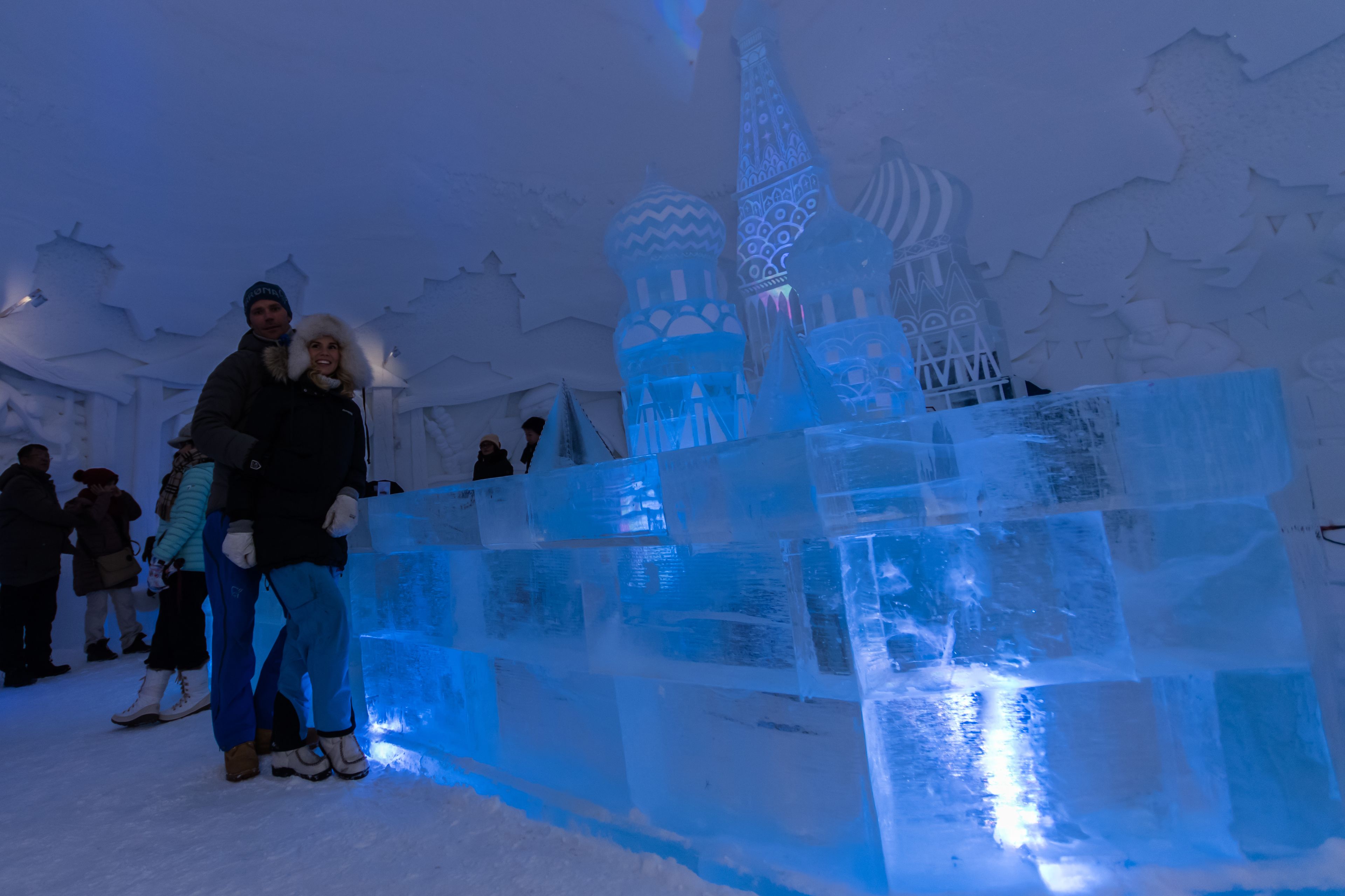 A large ice sculpture with a domed structure and a tower, surrounded by people.