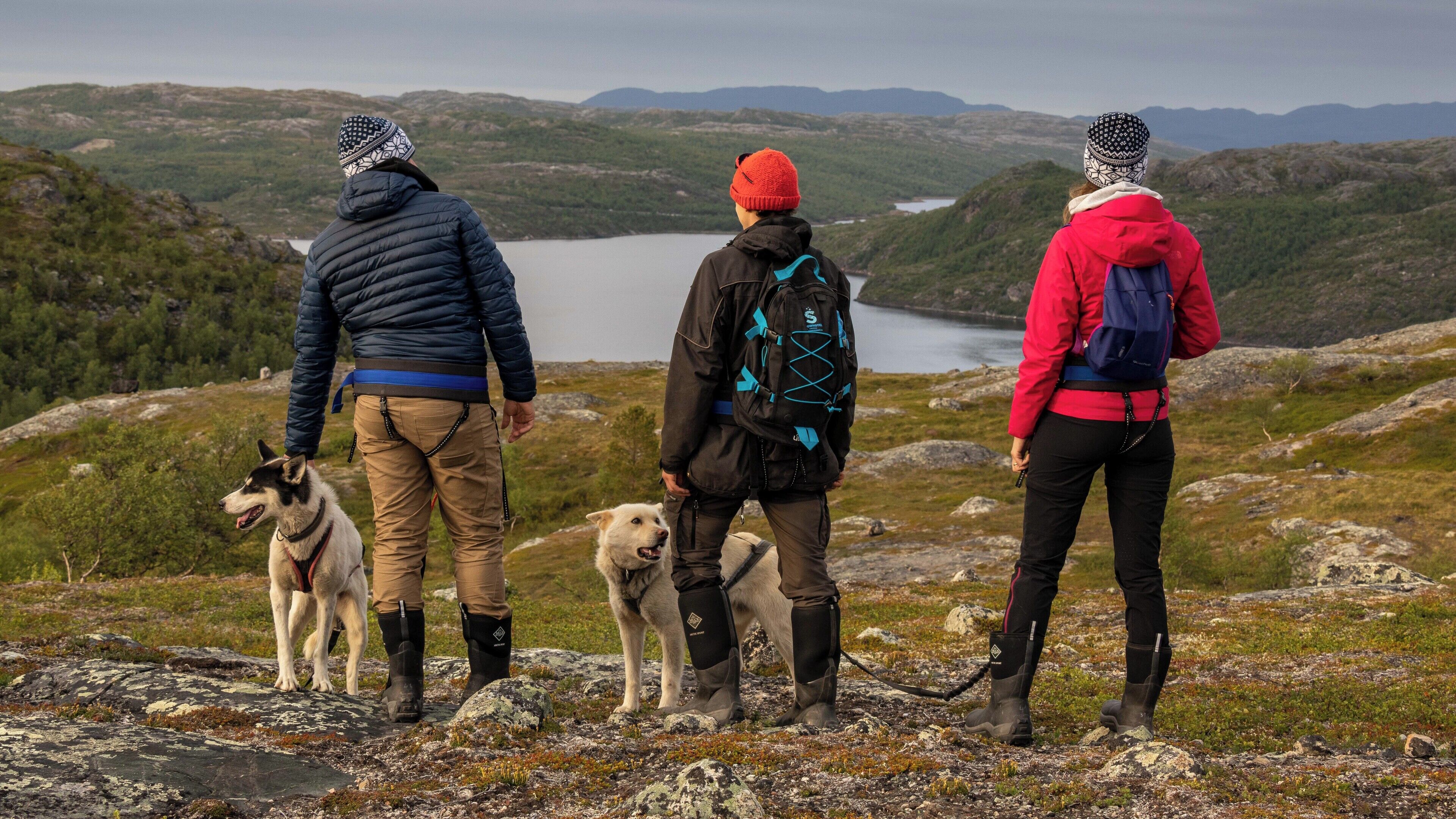 Tres personas sobre un terreno rocoso con un lago y montañas al fondo.