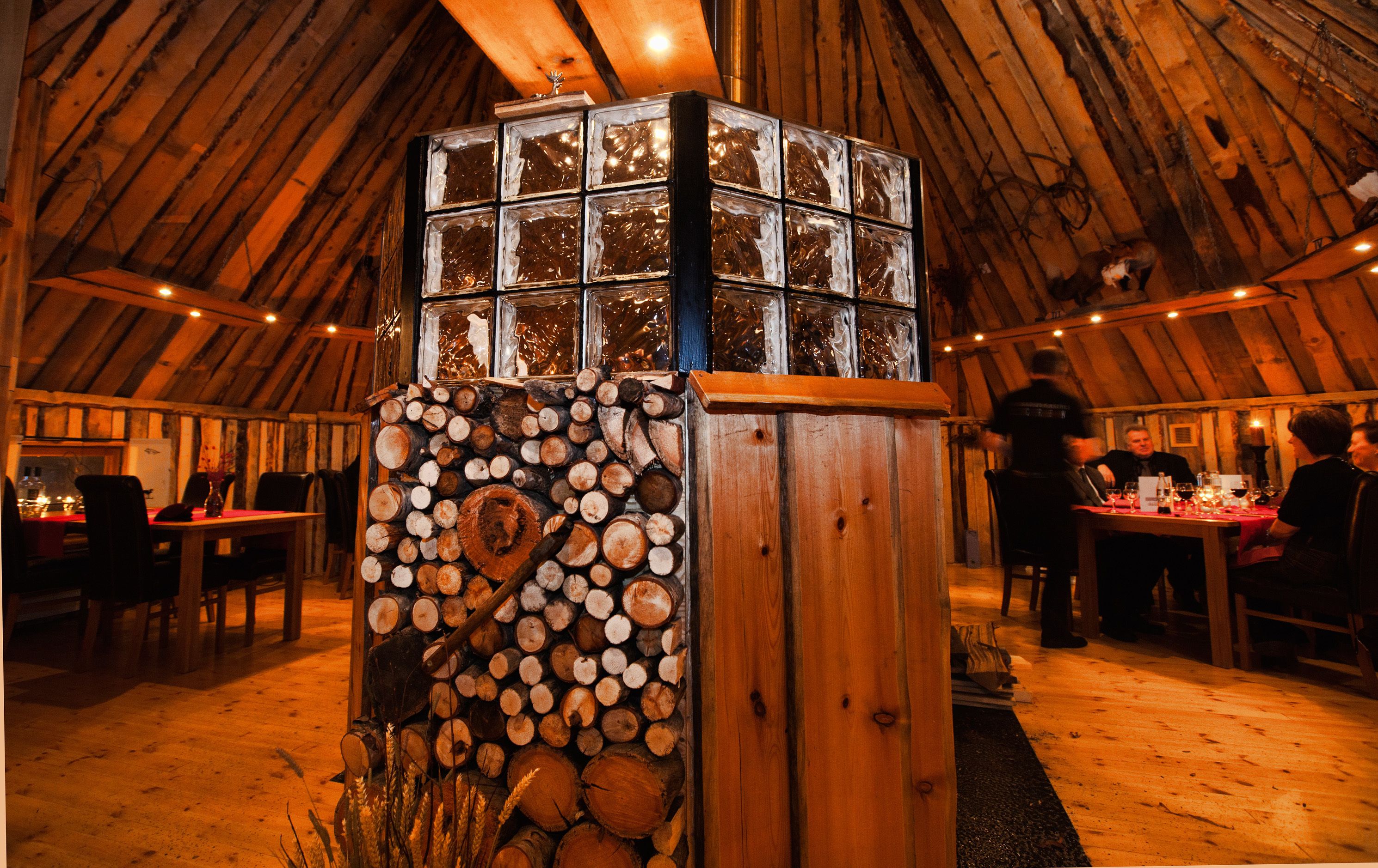 Eine rustikale Holzkonstruktion mit Glastisch, umgeben von einer Essecke mit Tischen und Stühlen.