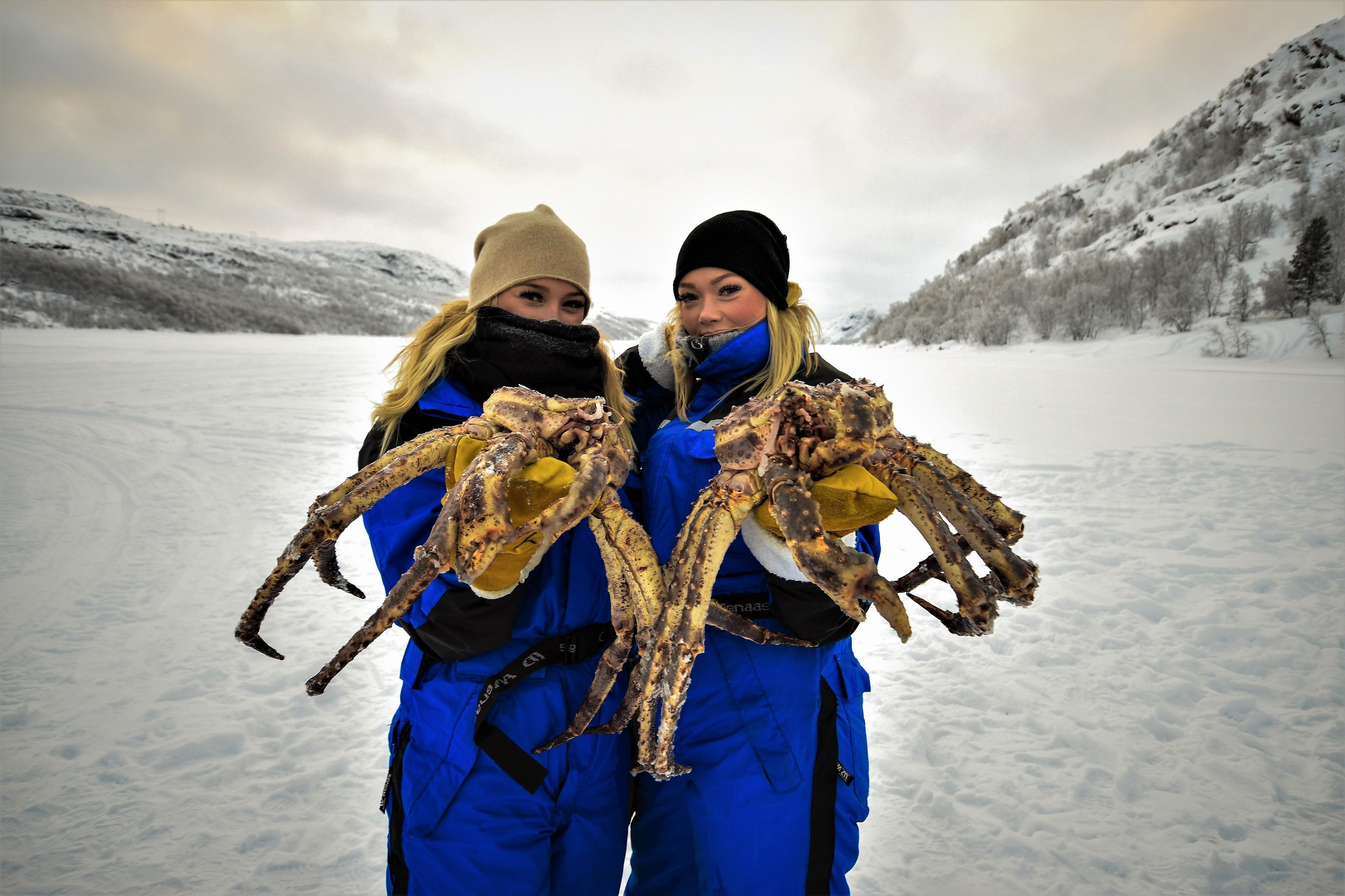 Two individuals holding large crabs in a snowy outdoor setting.
