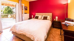 A bedroom with a large bed, a nightstand, a desk with a lamp, and a view of the outdoors. - Antonela Sunshine Apartment by CorfuEscapes (Corfu)