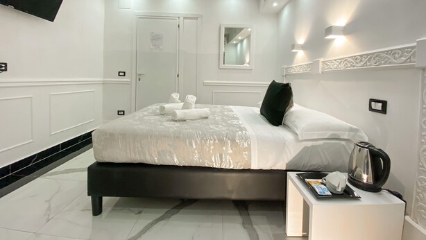 A modern hotel room with a large bed, a bedside table with a kettle, and a flat-screen TV mounted on the wall. - Locanda Parlamento (Rome)