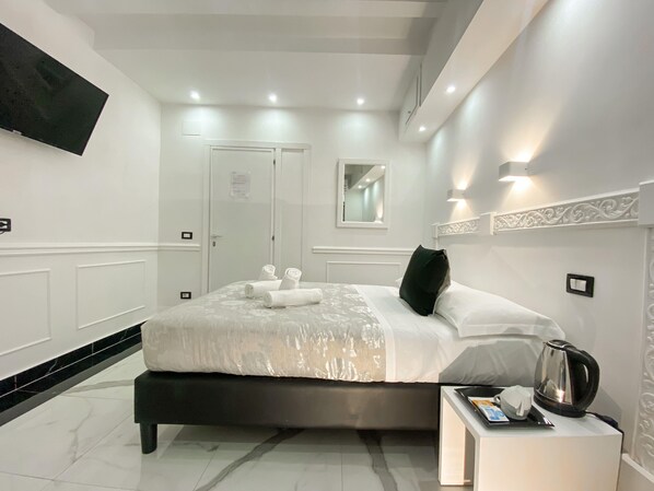 A modern hotel room with a large bed, a bedside table with a kettle, and a flat-screen TV mounted on the wall. - Locanda Parlamento (Rome)