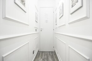 Un estrecho pasillo con paredes blancas y suelo de madera, que conduce a una puerta cerrada.