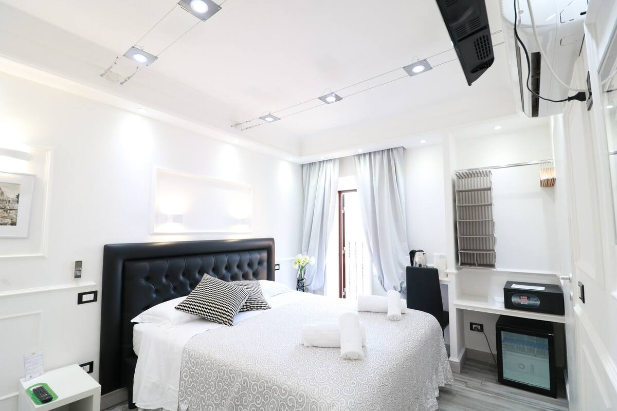 A modern hotel room with a large bed, bedside tables, a desk, and a built-in TV.