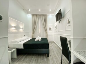 Una habitación de hotel con una cama, televisión montada en la pared, una silla y una mesita.