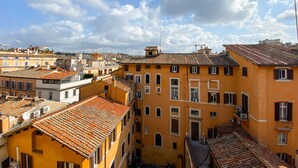 A view of a densely packed urban area with terracotta-tiled buildings and a clear blue sky with scattered clouds. - Locanda Parlamento (Rome)