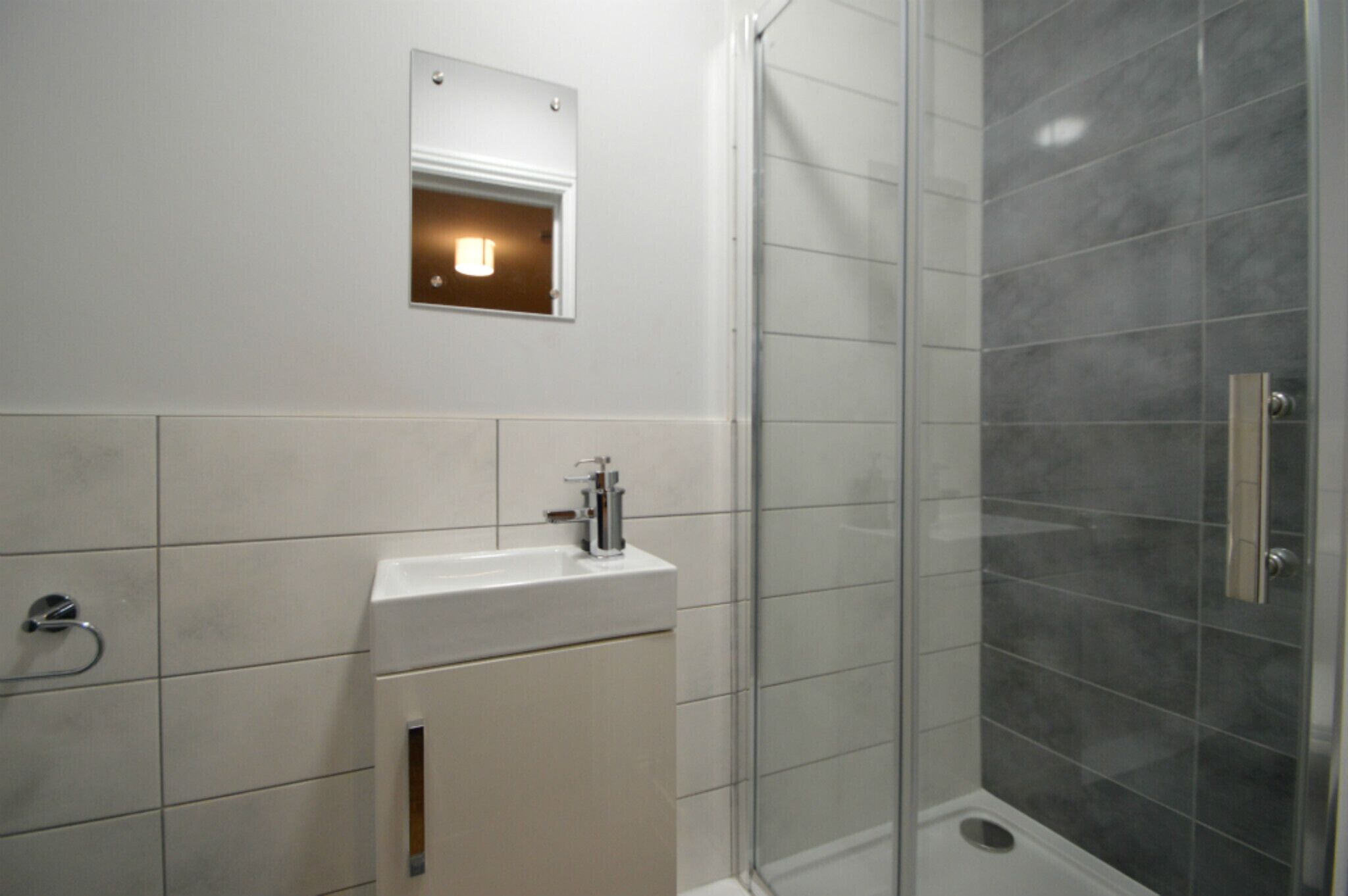 A bathroom with a white sink, a mirror, and a shower with grey tiles.