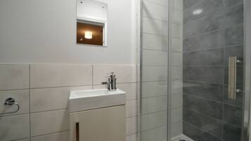 Een badkamer met een wit wastafelmeubel, een spiegel en een douche met grijze tegels.