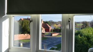 A window with three panes, each with a handle, overlooking a residential street with houses and greenery. - The Plough Retreat (Newark)