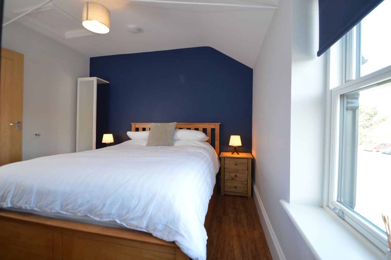 Een slaapkamer met een groot bed, twee nachtkastjes met lampen, een houten hoofdeinde en een raam met uitzicht.