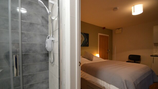 A bathroom with a shower and a bed with a headboard. - The Plough Retreat (Newark)