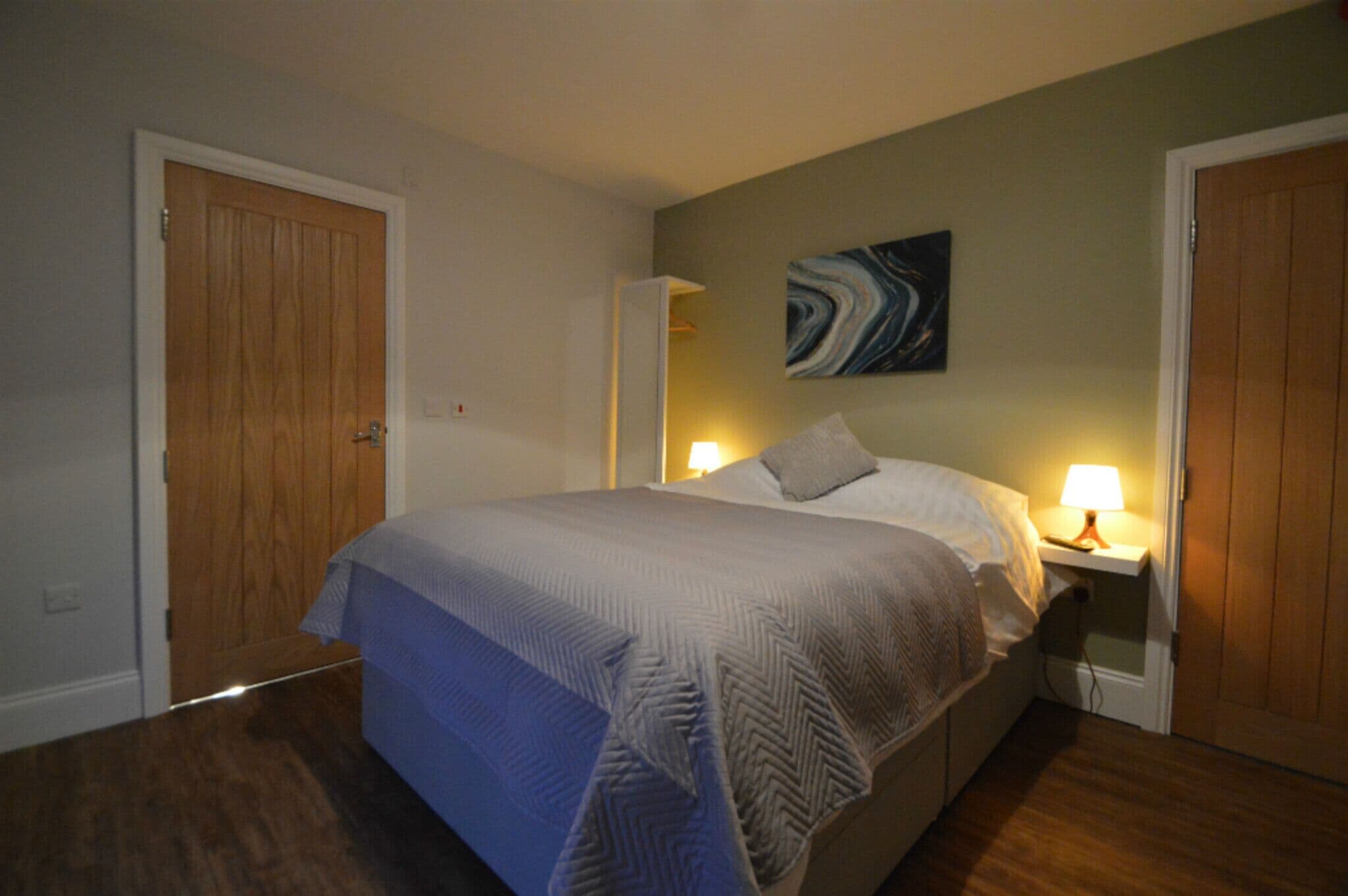 A bedroom with a large bed, two bedside lamps, and a painting on the wall.