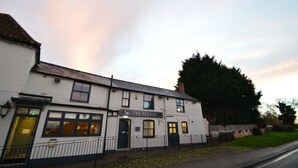 A white building with a sign reading "The Plough." It has a black roof, multiple windows, and a black fence in front. - The Plough Retreat (Newark)