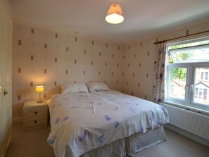 A bedroom with a bed, a nightstand, a lamp, and a window with curtains.