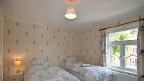 Un dormitorio con dos camas, una mesita de noche con lámpara, una ventana con cortinas y un radiador.