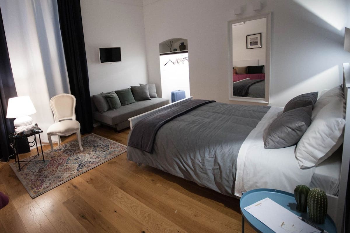 A modern bedroom with a large bed, a sofa, a chair, a desk, and a mirror.