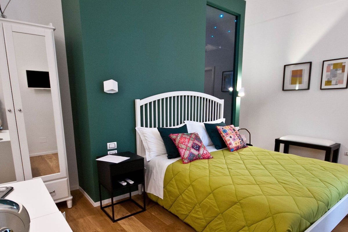 A bedroom with a white bed, green walls, a wooden floor, a white nightstand, and a white dresser.