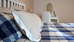 Een slaapkamer met een bed, kussens, een nachtkastje, een lamp en een spiegel.